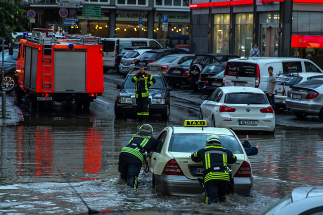 Feuerwehrleute schieben ein Auto von der überfluteten Straße