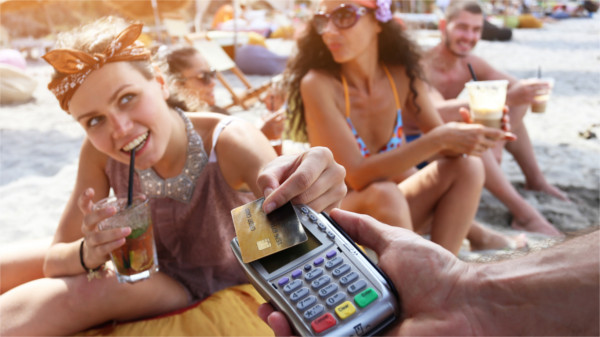 Junge Frauen trinken Cocktails am Strand und bezahlen mit der Kreditkarte